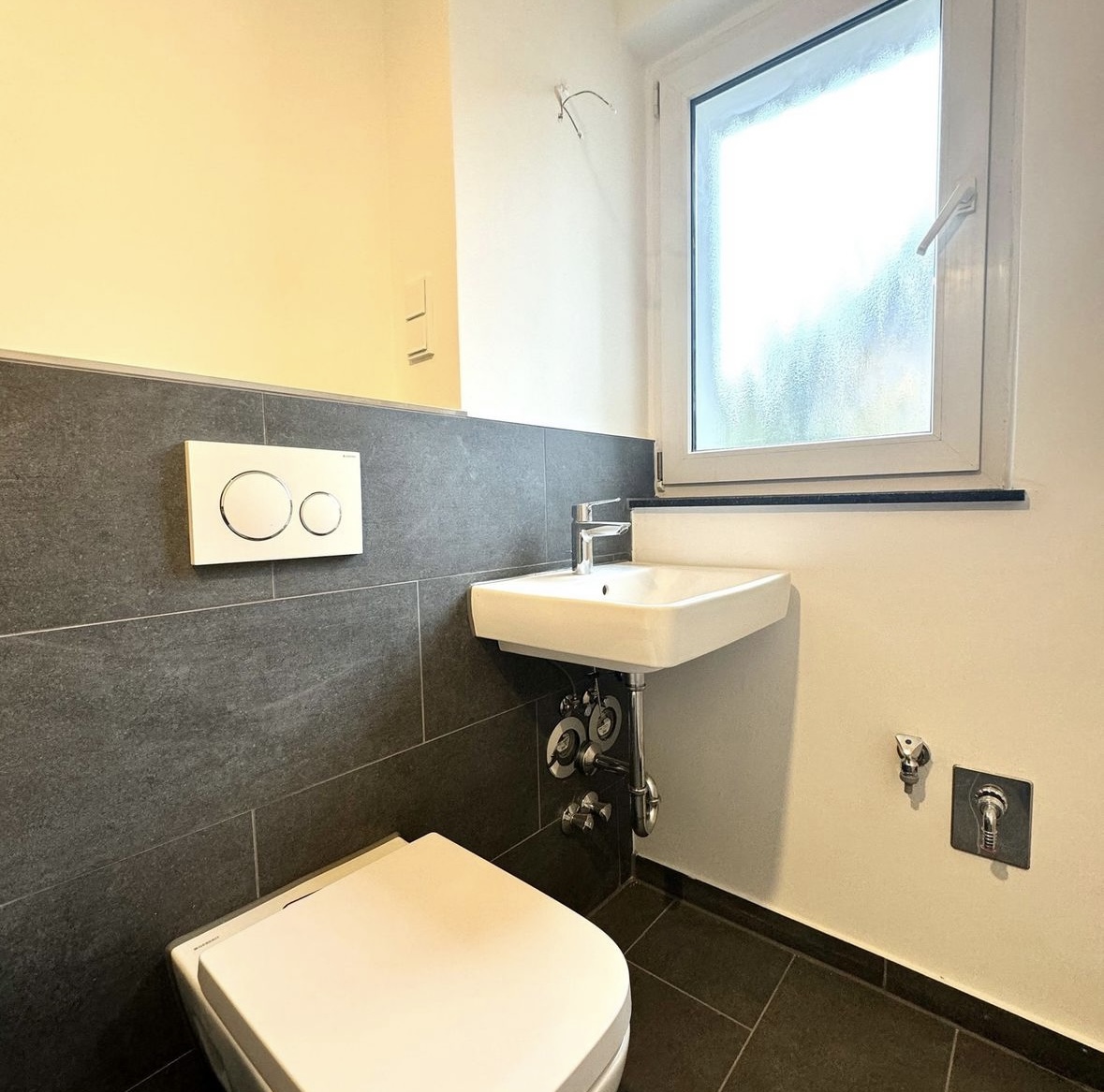 Wand-WC und Waschtisch vor anthrazitfarbener Fliesenwand in einem sanierten Bad in Berlin-Friedrichshain
