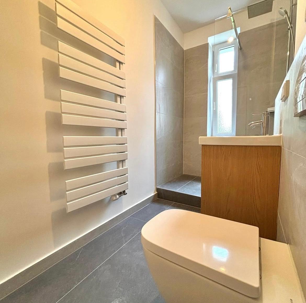 Schmales, komplett saniertes Badezimmer mit Wand-WC, Handtuchheizkörper und Holzelementen in Berlin-Mitte