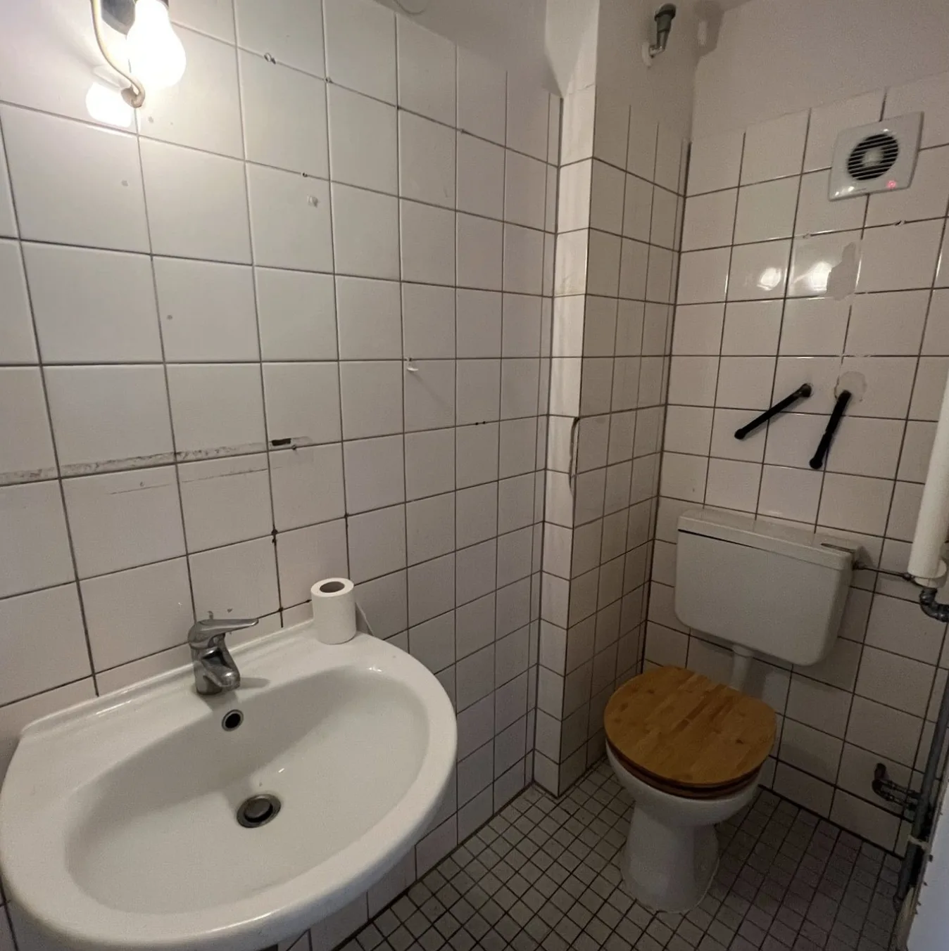 Ausgangszustand: weiß geflieste Wände, Mosaikboden und Stand-WC mit Aufputz-Spülkasten