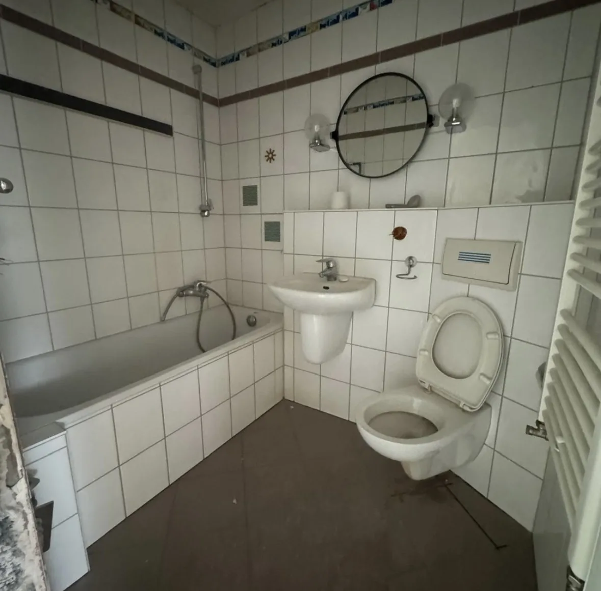 Ausgangszustand: weiß geflieste Wände mit Badewanne, Bordüre und Rundspiegel