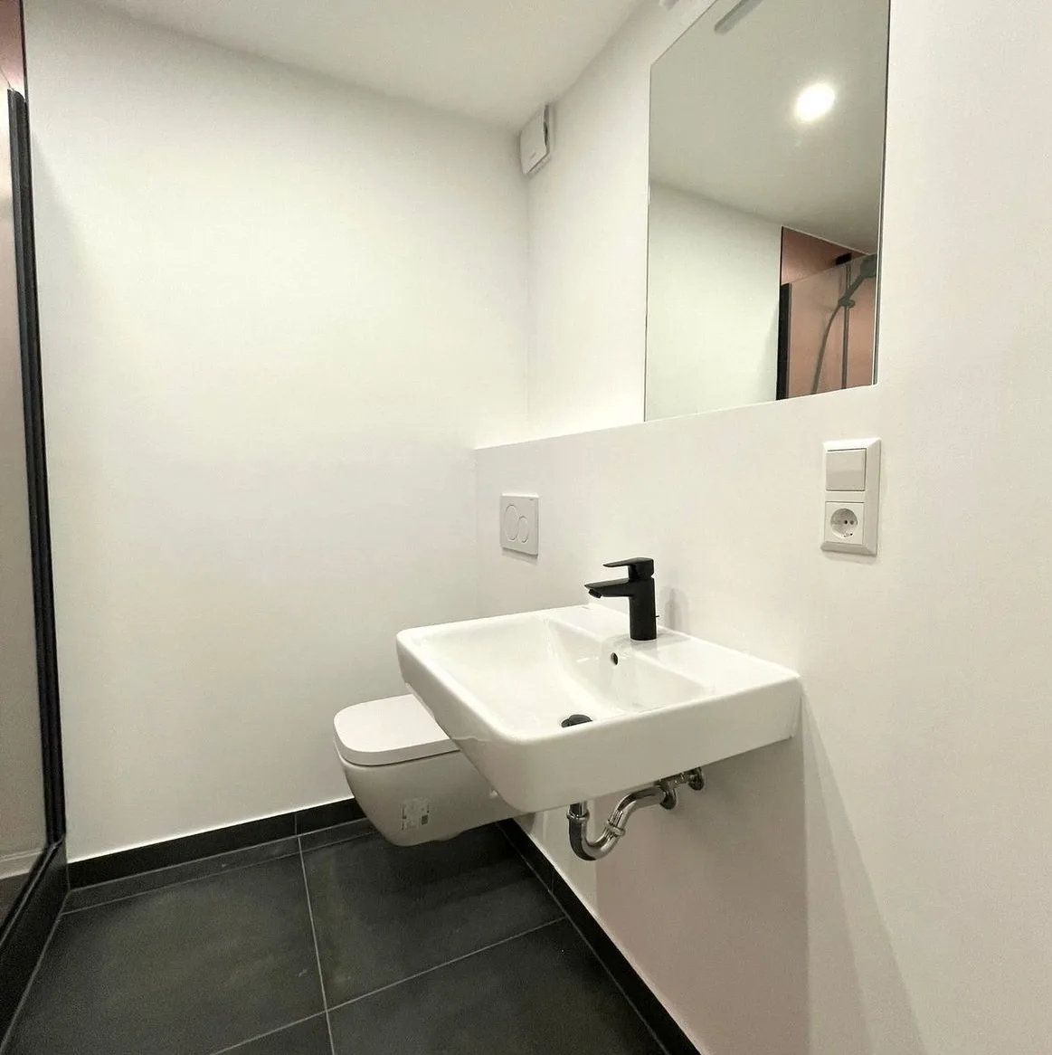 Waschbereich mit hohem Wandspiegel, Wand-WC und schwarzer Armatur